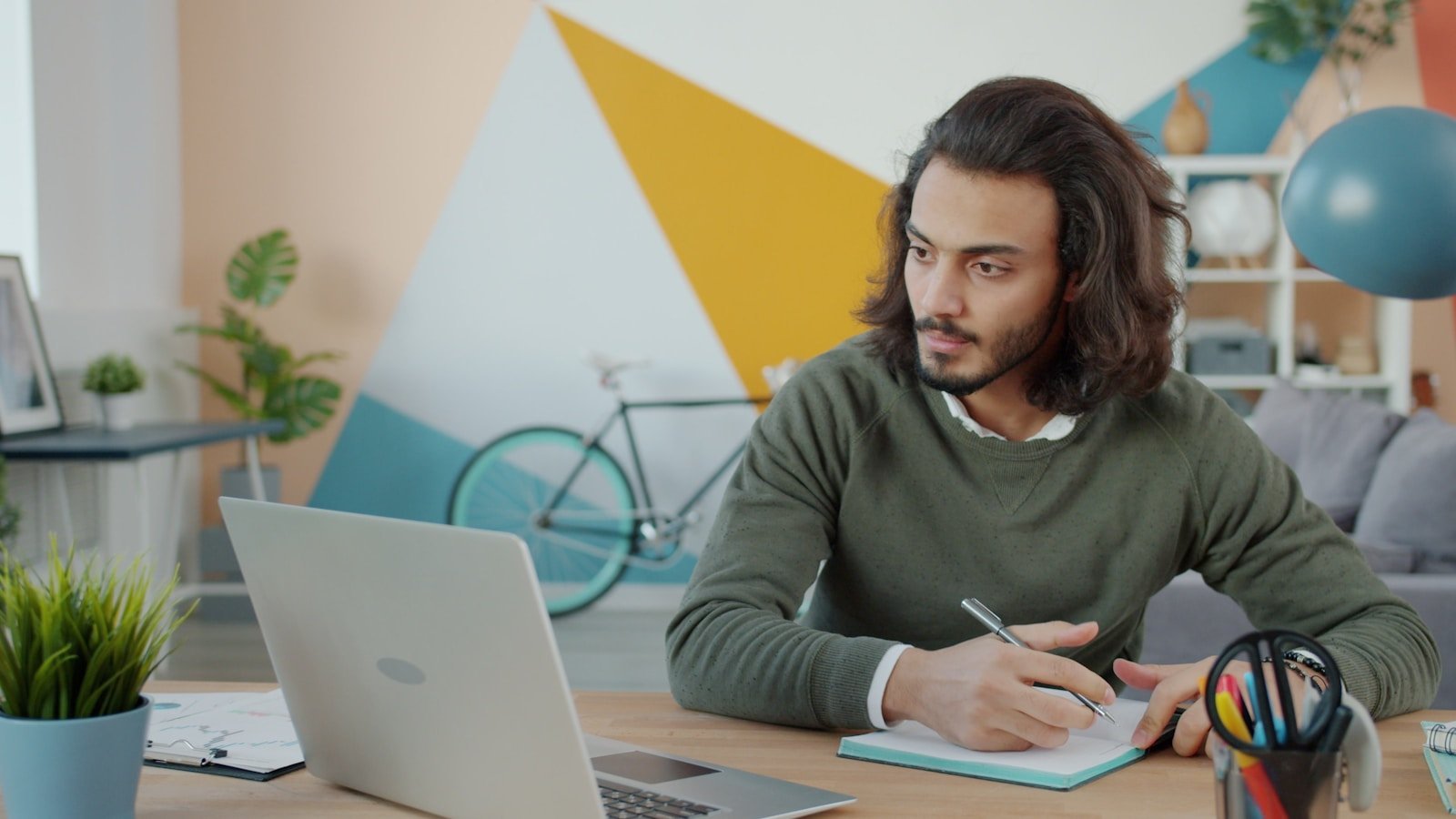 Professional taking notes beside a laptop to reverse outline a graduate paper